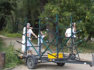 3 osoby stoją na pustej przyczepie na kajaki